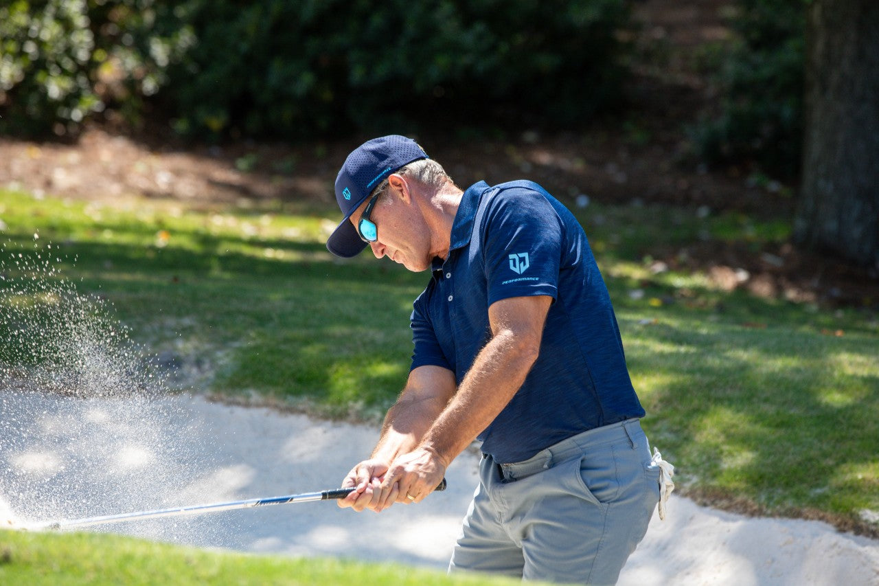 Side view of Dan Jansen hitting a bunker shot, sand flying as he wears Jansen Eyewear for clear vision